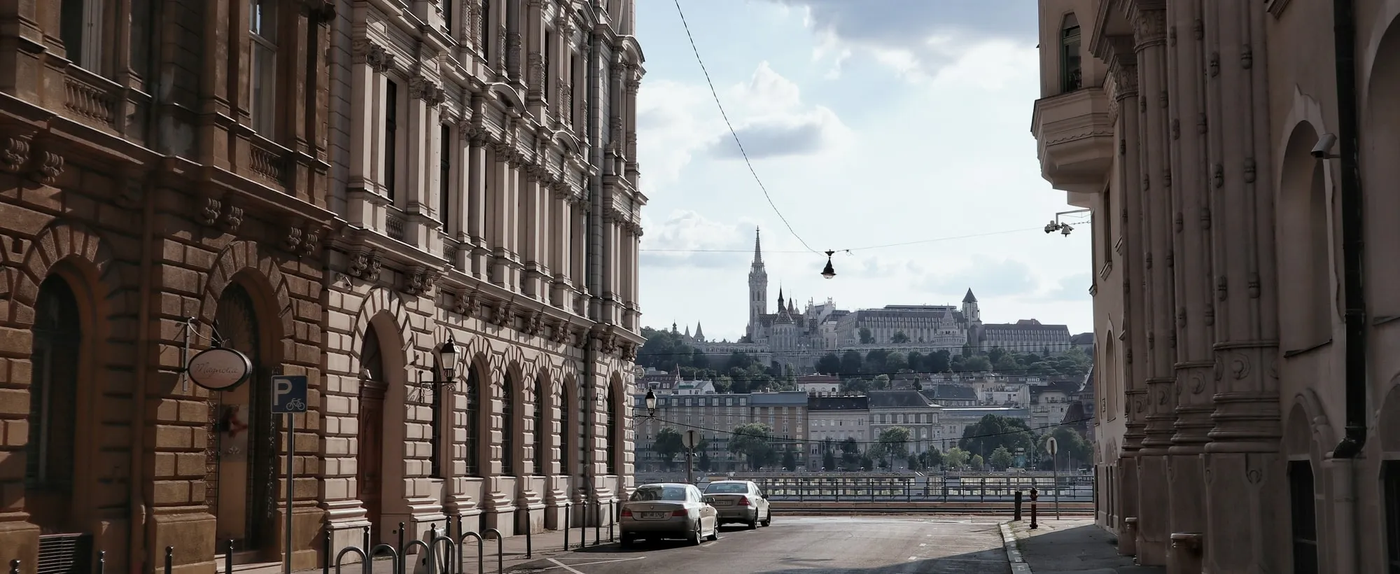 A Budapest street of old apartment buildings, with the towers of Castle Hill at the far end.